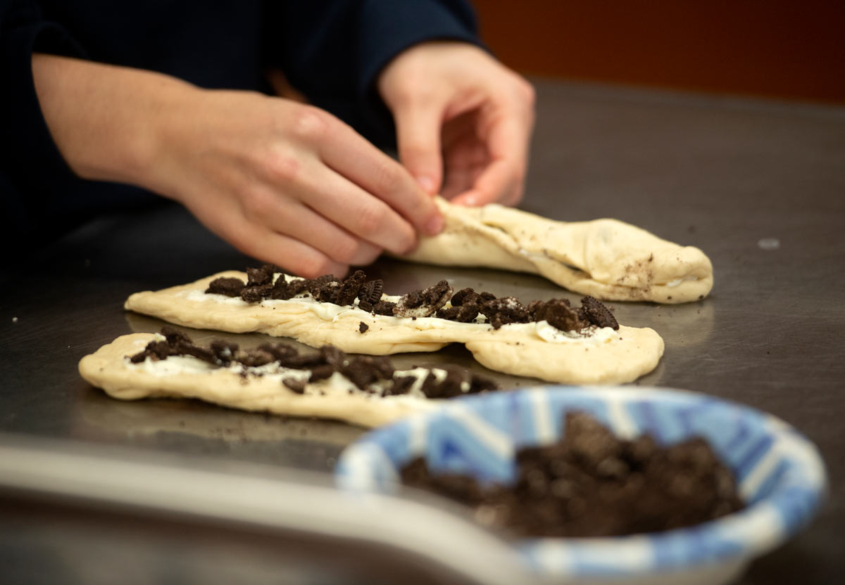 Hands work with three braids, adding Oreo cookie pieces.