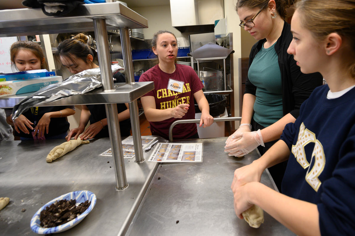 Female student gives instructions to other students in kitchen.