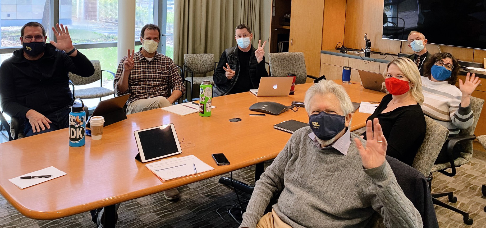 A group of people with COVID masks sit at a meeting table together