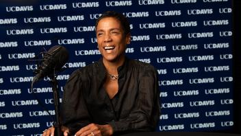 LeShelle May laughing with a microphone in front of her and a dark blue UC Davis background