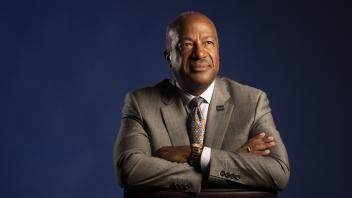 A portrait of Chancellor Gary May with crossed arms in front of a dark blue background