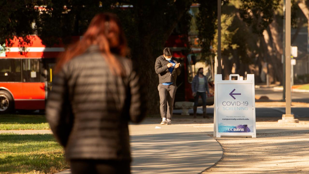 COVID-19 testing sign, students walking on sidewalk