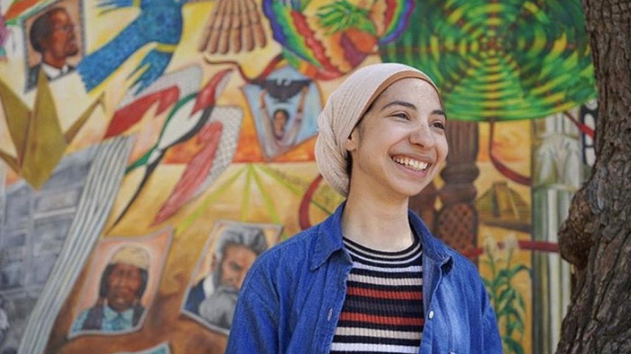 UC Davis student Nora Abedelal poses with a mural.