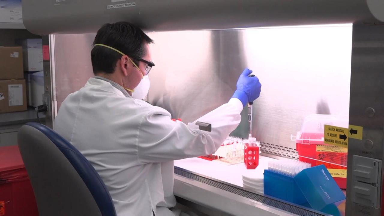 Man in laboratory gear holding COVID-19 test samples.