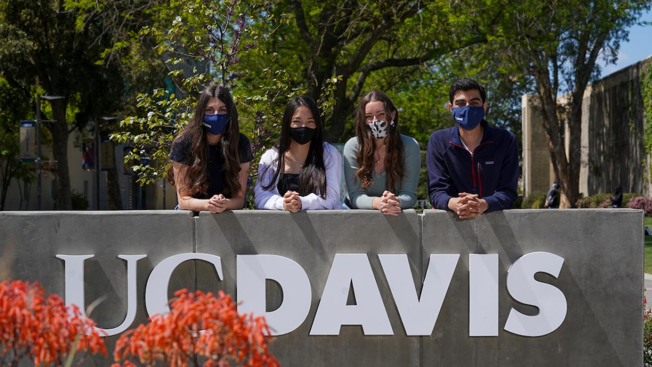 Four masked students at the UC Davis sign