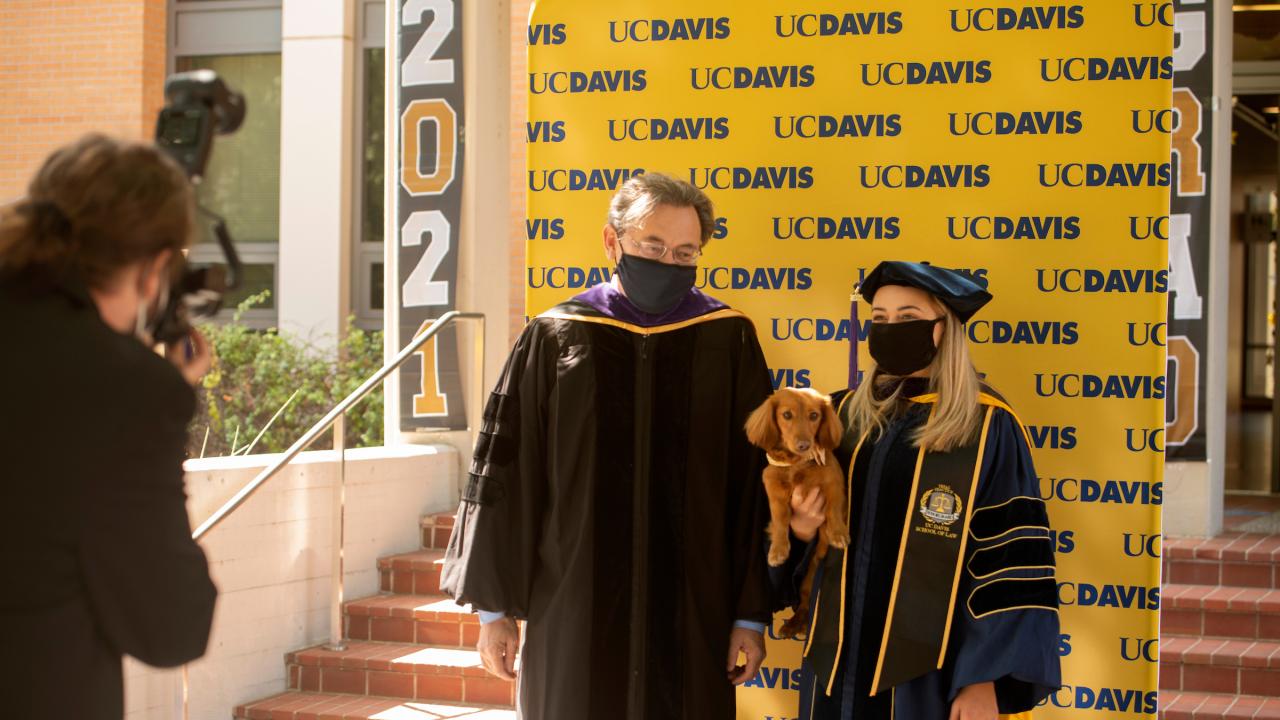 Dean of UC Davis Law school with graduate and puppy in front of UC Davis background.