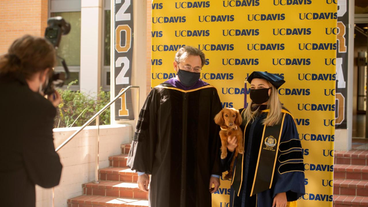 Dean of UC Davis Law school with graduate and puppy in front of UC Davis background.