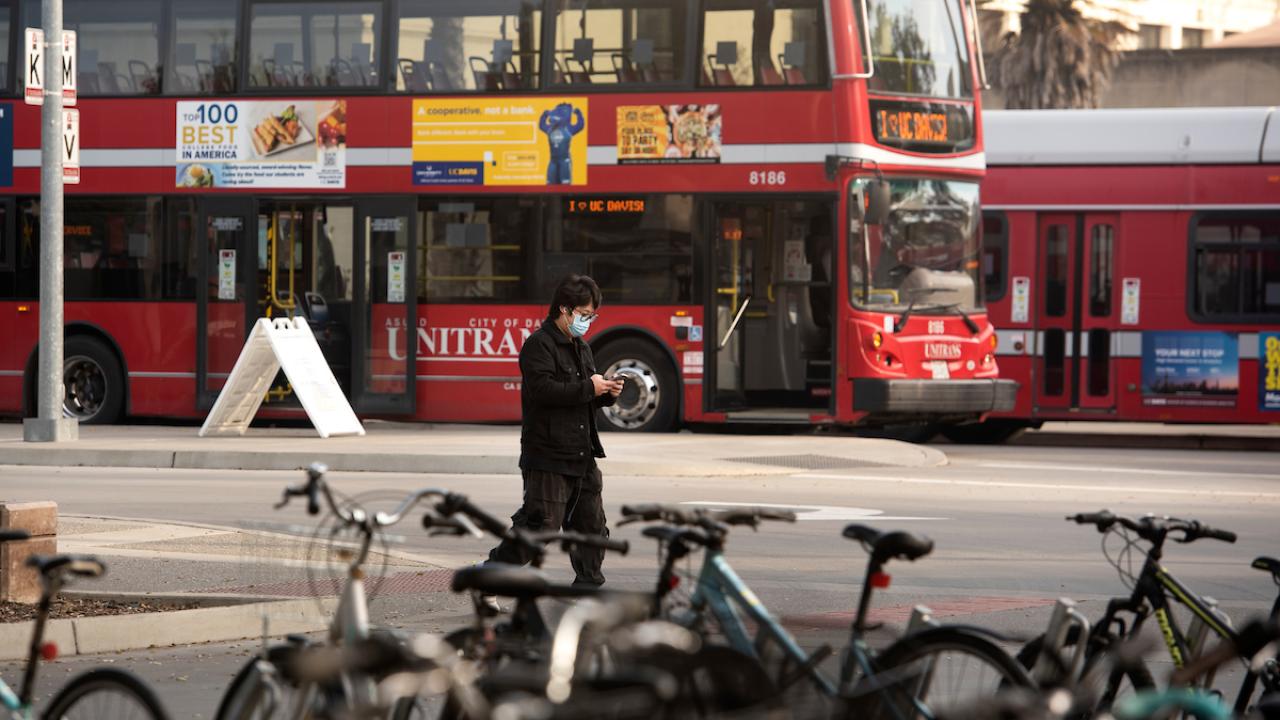 Masked person walking near Unitrans buses