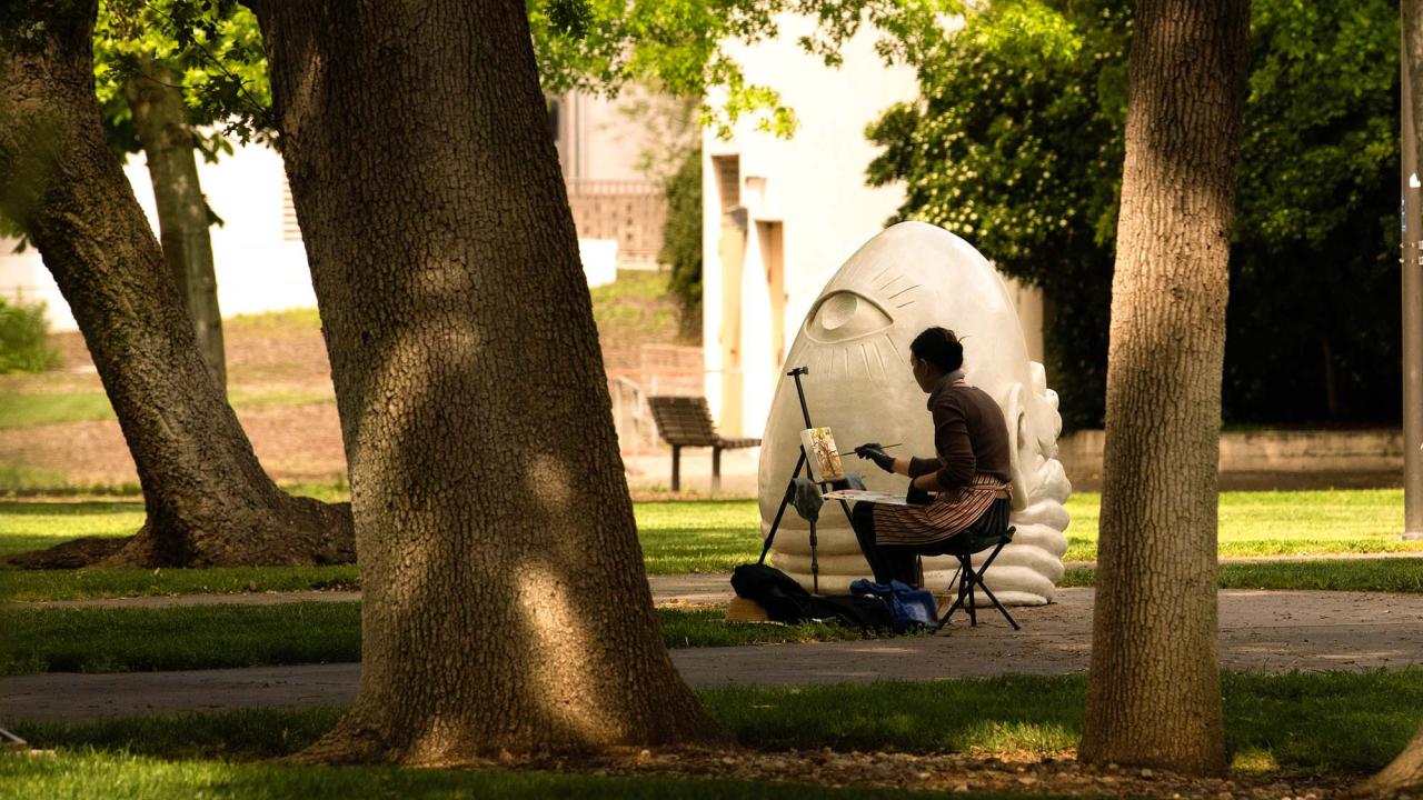 A photograph of a painter working on a canvas while near the statue of the Eye on Mrak sculpture.