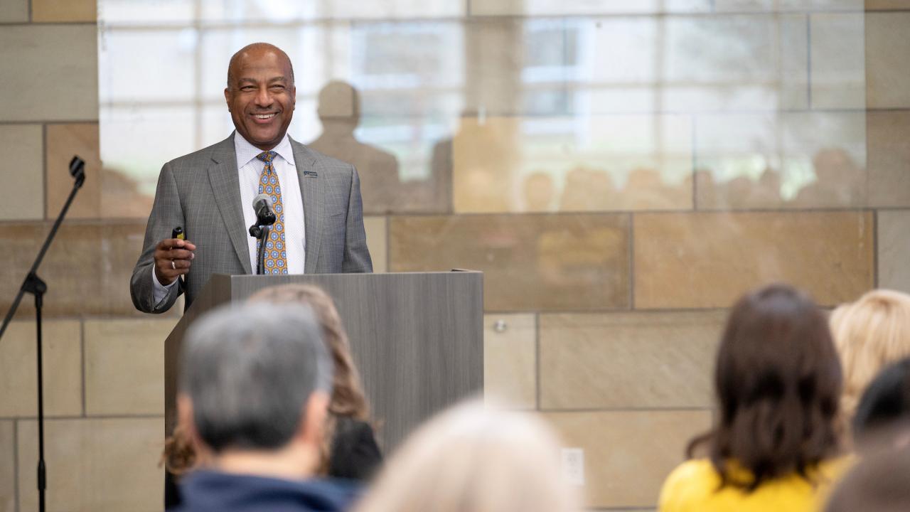 Chancellor Gary May wearing a gray suit and speaking into a microphone