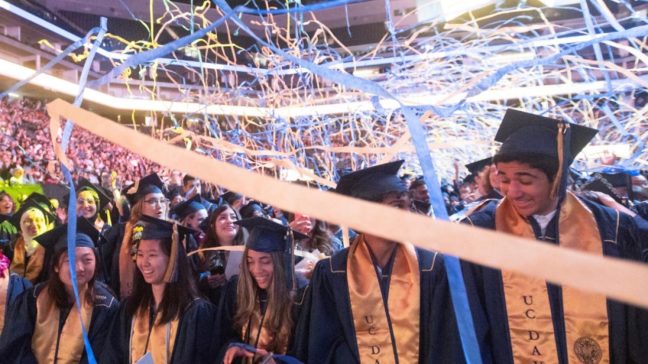 UC Davis students celebrate spring 2024 commencement with blue and gold streamers above them.
