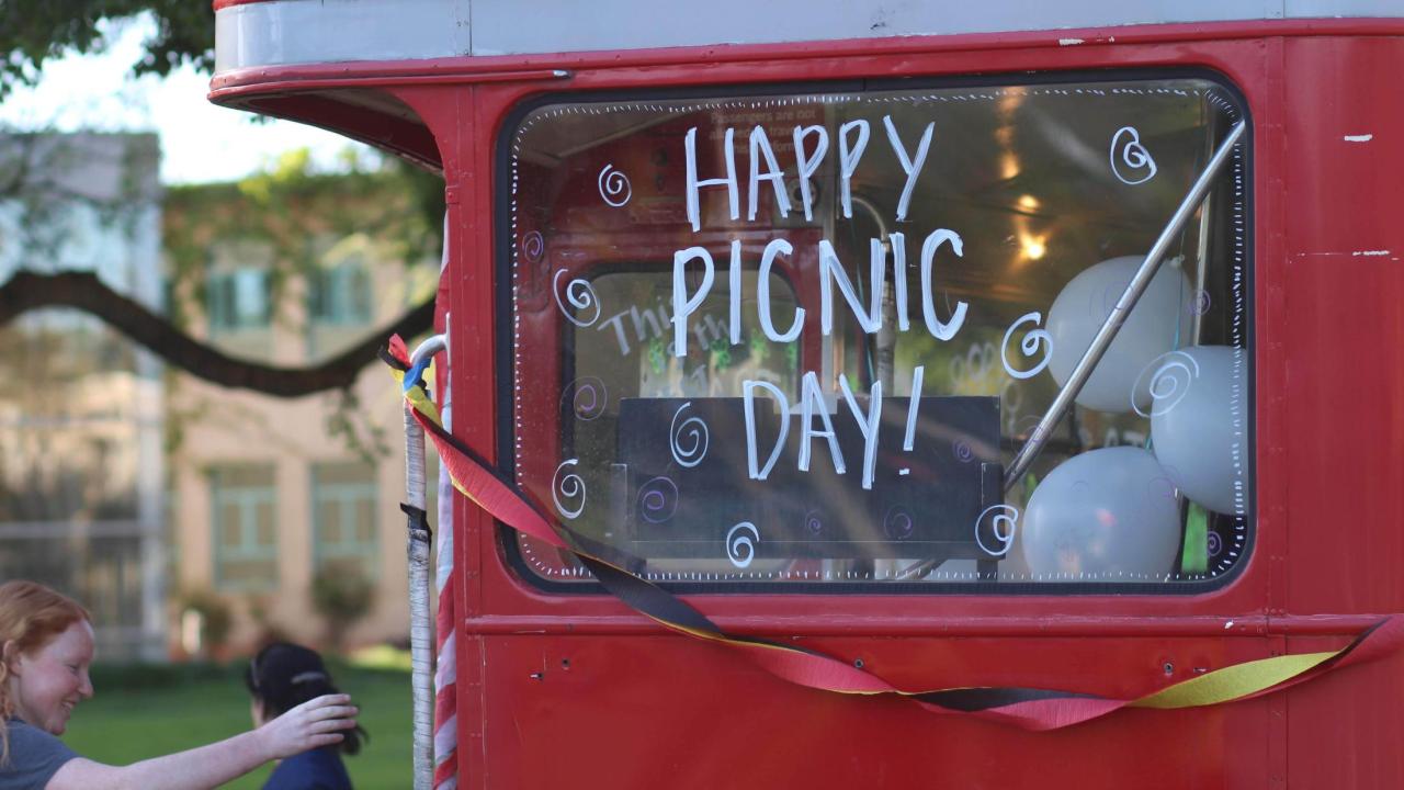 Red double decker bus with "Happy Picnic Day!" on the window