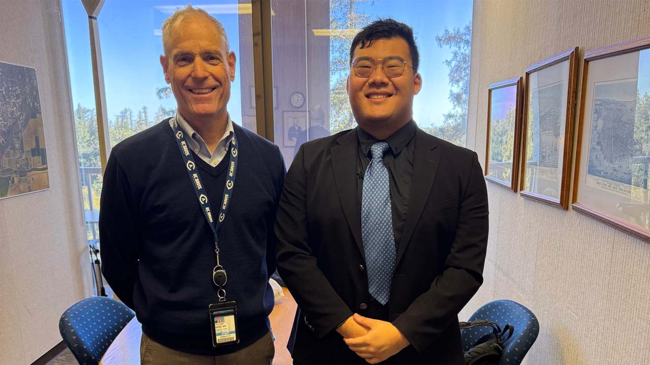 Two people pose for photo in meeting room, near window