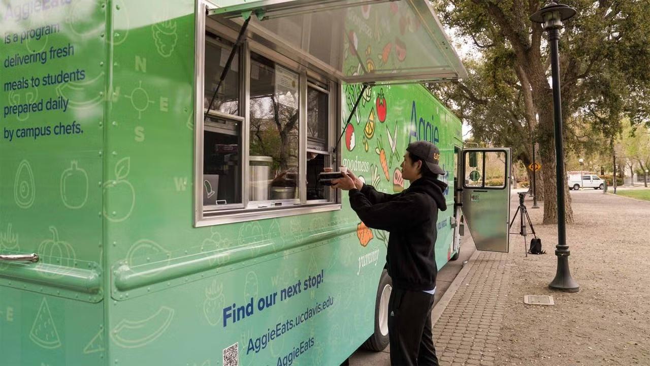 A student receiving an order of food in takeway containers from the Aggie Eats food truck