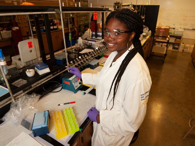 Female student in lab coat looking into the camera in a biochemistry laboratory.