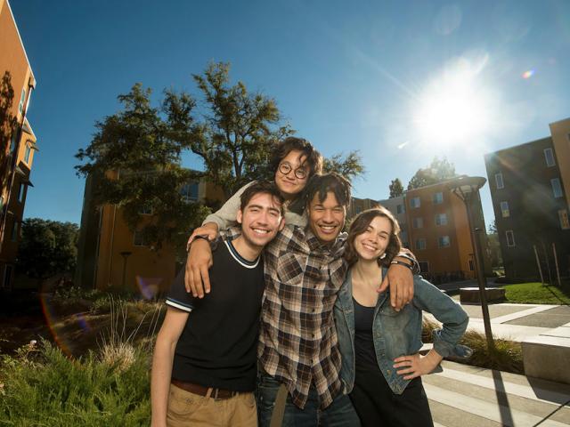 A group of UC Davis Students smiles in front of on campus housing