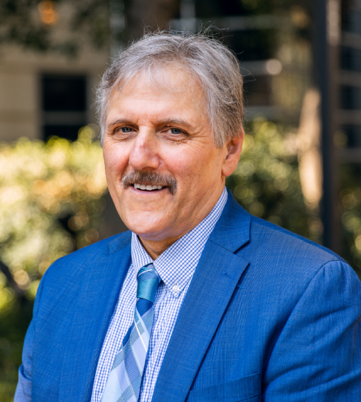 Dean Richard L. Corsi looking at camera smiling, wearing blue suit.