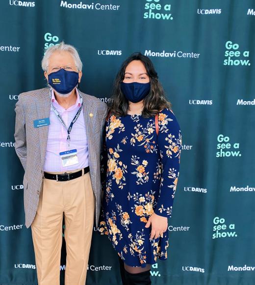 Two people stand against a Mondavi Center blue background