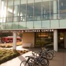 Student Health and Counseling Services Center building with bike racks, bus and person riding a bike 