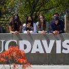 Four masked students at the UC Davis sign