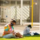 Two students wearing masks studying on lawn.