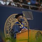 Chancellor May speaking at graduation behind podium in commencement regalia 