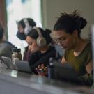 Students look at computer and phone screens while seated at a counter in a dining facility on campus.