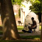 A photograph of a painter working on a canvas while near the statue of the Eye on Mrak sculpture.