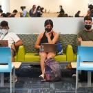 Three students with masks on use their  laptops while sitting on a couch in the Memorial Union.