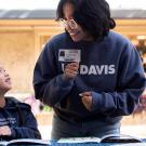 A college student smiling down at an elementary student reading a book.
