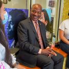 Chancellor Gary S. May talks with two students, seated, inside the Student Community Center